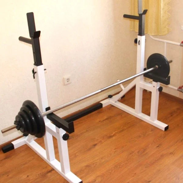 White weight bench with barbell on a wooden floor against a beige wall.