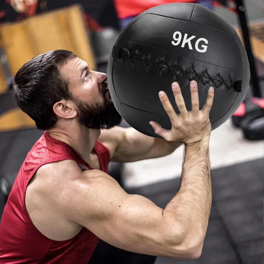 Man lifting a 9KG medicine ball in a gym setting